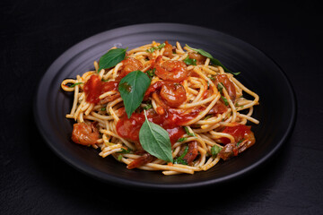 Poster - Delicious spaghetti pasta with prawns and cheese served on a black plate. With vegetables, Italian tomato sauce, and spices arranged on a wooden table, black background, top view