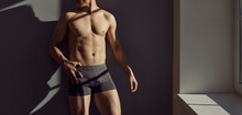 Wide Narrow Banner Of Sexy Naked Man In Briefs On Grey Wall Background. Toned Active Sporty Guy In Underwear Advertise Good Quality Underclothing Garment. Crop. Fashion Advertisement.