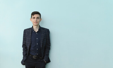 Stylish young guy standing near blue wall looking at camera smiling, place for text