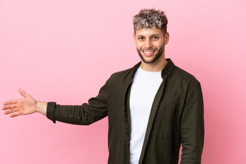 Wall Mural - Young handsome caucasian man isolated on pink background extending hands to the side for inviting to come