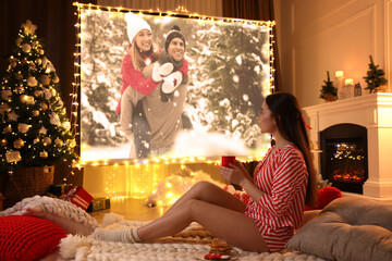 Sticker - Woman with cup of hot drink watching romantic movie via video projector in room. Cozy winter holidays atmosphere