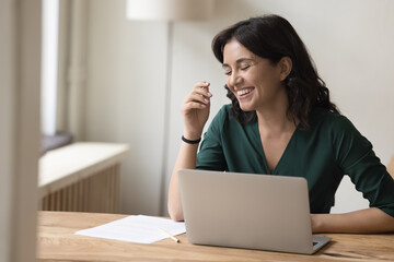 Wall Mural - Happy Asian millennial employee woman in casual having fun at workplace table, laughing at laptop computer, enjoying work on business project, job tasks, online communication