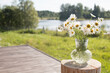 Bouquet of daisies in a vase against the backdrop of a lake in the sun.