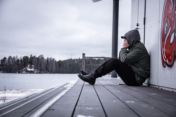 Wall Mural - Depressed hooded man sitting and covering his face into his arms