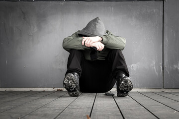 Wall Mural - Depressed hooded man sitting and covering his face into his arms