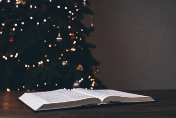 Wall Mural - An open Bible on the table. Prayer. Christmas background. Candles, lights and garlands