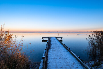 Wall Mural - Snow covered jetty at a lake in the Netherlands during a winter sunset