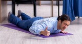 Fototapeta  - Young handsome businessman doing exercises at workplace
