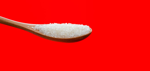 Wooden spoon with sugar crystals on red background