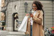 © Kostiantyn - Fashion afro american woman after shopping with paper bags standing in city and using phone