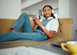 © Kay A/peopleimages.com - Relax, phone and woman on a sofa with music, radio and online entertainment in a living room, happy and content. Podcast, student and girl with smartphone on a couch, rest and break in Brazil home