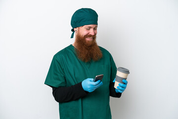 Wall Mural - Surgeon redhead man in green uniform isolated on white background holding coffee to take away and a mobile