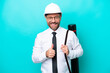 © luismolinero - Middle age architect man with helmet and holding blueprints isolated on blue background giving a thumbs up gesture