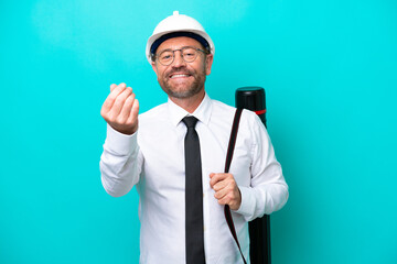 Wall Mural - Middle age architect man with helmet and holding blueprints isolated on blue background making money gesture