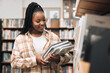 © K Abrahams/peopleimages.com - Black woman, university student and library with books for education, learning and knowledge at campus. Happy, smile and gen z college student at bookshelf for studying, academic research and reading