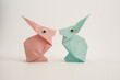 pastel pink and green  paper origami hares rabbits with googly eyes meeting  isolated on a white background