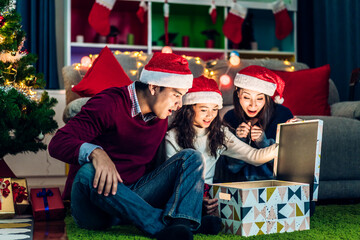 Portrait of happy family father and mother with daughter in santa hats having fun opening magic christmas gift box and enjoying spending time together in christmas time at home