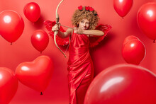 Serious Woman In Role Of Cupid Shoots Arrow Wears Elegant Dress Tries To Find Love Brings Happiness To All Has Ability To Make People Fall In Love With Each Other Poses Around Heart Shaped Balloons