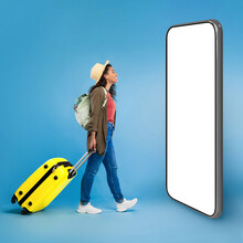 Happy Young Black Woman Walking With Suitcase, Checking Smartphone Screen