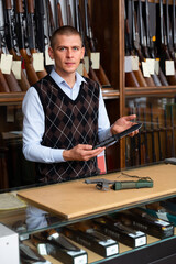 Wall Mural - Serious gunsmith shop assistant demonstrates hunting knife in his hands