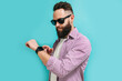 Portrait of a positive handsome bearded man, wearing a smart watch and casual clothes on a blue studio background