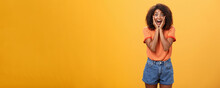 Impressed Talkative African American Woman Finding Out Hot Details Of Rumor Being Excited, Thrilled Leaning Face On Palms, Smiling Broadly With Amused Expression Listening Carefully Over Orange Wall