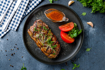 Poster - juicy Striploin Steak with tomato sauce and vegetables on black plate top view