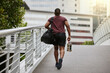© S Fanti/peopleimages.com - Fitness, city or black man walking to gym on a bridge with a sports bag or water bottle for a workout or exercise. Back view, motivation or healthy person traveling to a training center or club