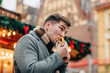 © Westend61 - Young man eating hot dog standing at Christmas market