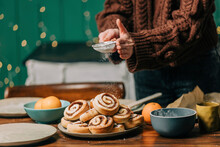Hands of woman sprinkling powdered sugar on cinnamon buns at home