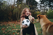 Cute Girl Holding Soccer Ball Playing With Dog At Park