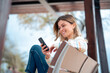© Westend61 - Smiling beautiful young woman sitting on bench using mobile phone