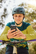 © Clement C/peopleimages.com - Mountain bike, phone and man outdoor in nature forest while online with a smile for communication or watching stunt video on internet. Athlete male with bicycle and smartphone for sports training