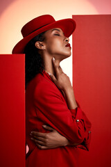 Wall Mural - Fashion, model and black woman in studio for creative, clothes and posing in power suit on red background. Fashion model, girl and elegant clothing by designer with vision, classic and sexy aesthetic