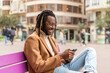 © Renata Hamuda - Handsome smiling man sits on a bench in the city and uses his phone