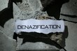 Paper with word Denazification on pieces of concrete, top view