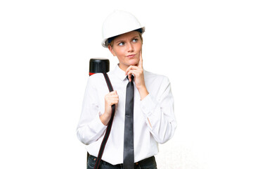 Wall Mural - Young architect caucasian woman with helmet and holding blueprints over isolated background having doubts and with confuse face expression
