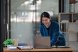 © Songsak C - Young Asian businesswoman standing at her office desk and working on her laptop with happiness.