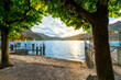 View from the lakefront Lungolago Europa promenade near a small pier looking across the lake at the mountains and Lake Como at sunset in the town of Bellagio, Italy.
