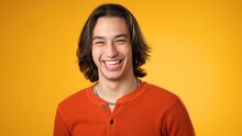 Portrait Of Smiling Laughing, Happy, Handsome Hispanic Gender Fluid Young Man 20s Wearing Orange Casual Shirt Isolated On Yellow Color Background In Studio. Sincere Emotions Lifestyle Concept.