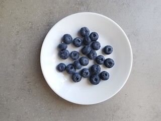 Wall Mural - White dish of lush blueberries against grey neutral coloured background