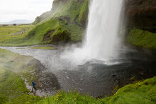 A Man Walks Away From Seljalandsfoss Waterfall.; Seljalandsfoss, Iceland