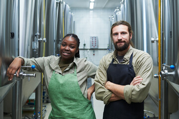 Positive diverse team of microbrewery workers standing among equipment for fermentation