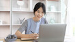 © Puwasit Inyavileart - Asian woman taking notes in notebook while studying online in laptop at home, Video chat, Online communication , Stay home, New normal, Distance learning.., Social distancing, Learn online...