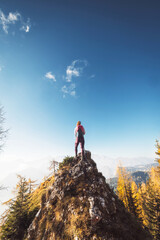 Vertical photo, back view of woman hiker standing on top of the rock on a sunny autumn day looking at the view from high up