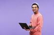 © pressmaster - Young successful designer or freelancer in casualwear using laptop and looking at camera with smile while standing on violet background