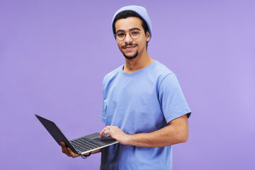 Aufkleber - Young successful student or designer in blue t-shirt and beanie hat holding laptop while looking at camera against lavender background