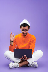 Aufkleber - Young man looking at laptop screen with astonishment while sitting in front of camera with his legs crossed and networking