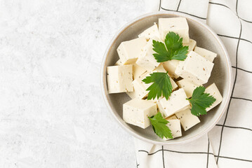 Tofu soy cheese or paneer or feta cheese cubes adding fresh parsley and celery in a ceramic bowl on a checkered napkin isolated top view