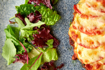 Canvas Print - Tasty pork chop oven baked with tomatoes and cheese served on gray plate with fresh greens.